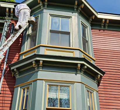 A Prusik painter is on a ladder painting a beautiful exterior of a townhouse in Boston.